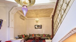 A living room with a sofa set, a dining table with fruit, and a patterned rug.