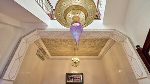 A room with a high ceiling, ornate ceiling design, a chandelier, and a framed artwork on the wall.