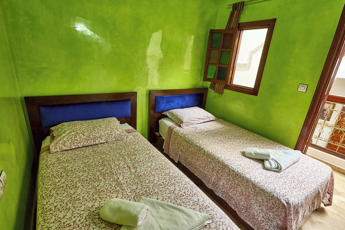 A room with two single beds, each with a patterned bedspread and pillows, against a green wall.