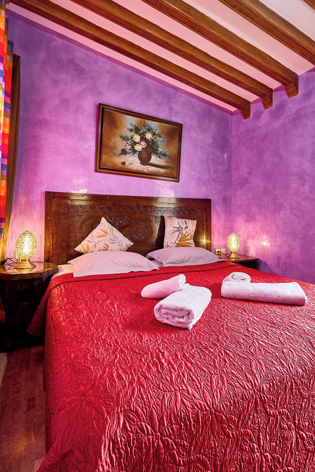 A hotel room with a large bed, a wooden headboard, a painting above the bed, and two bedside lamps.