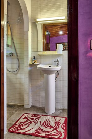 A bathroom with a white sink, a shower, and a red and white rug. - Riad Amber Zahra (Marrakech)