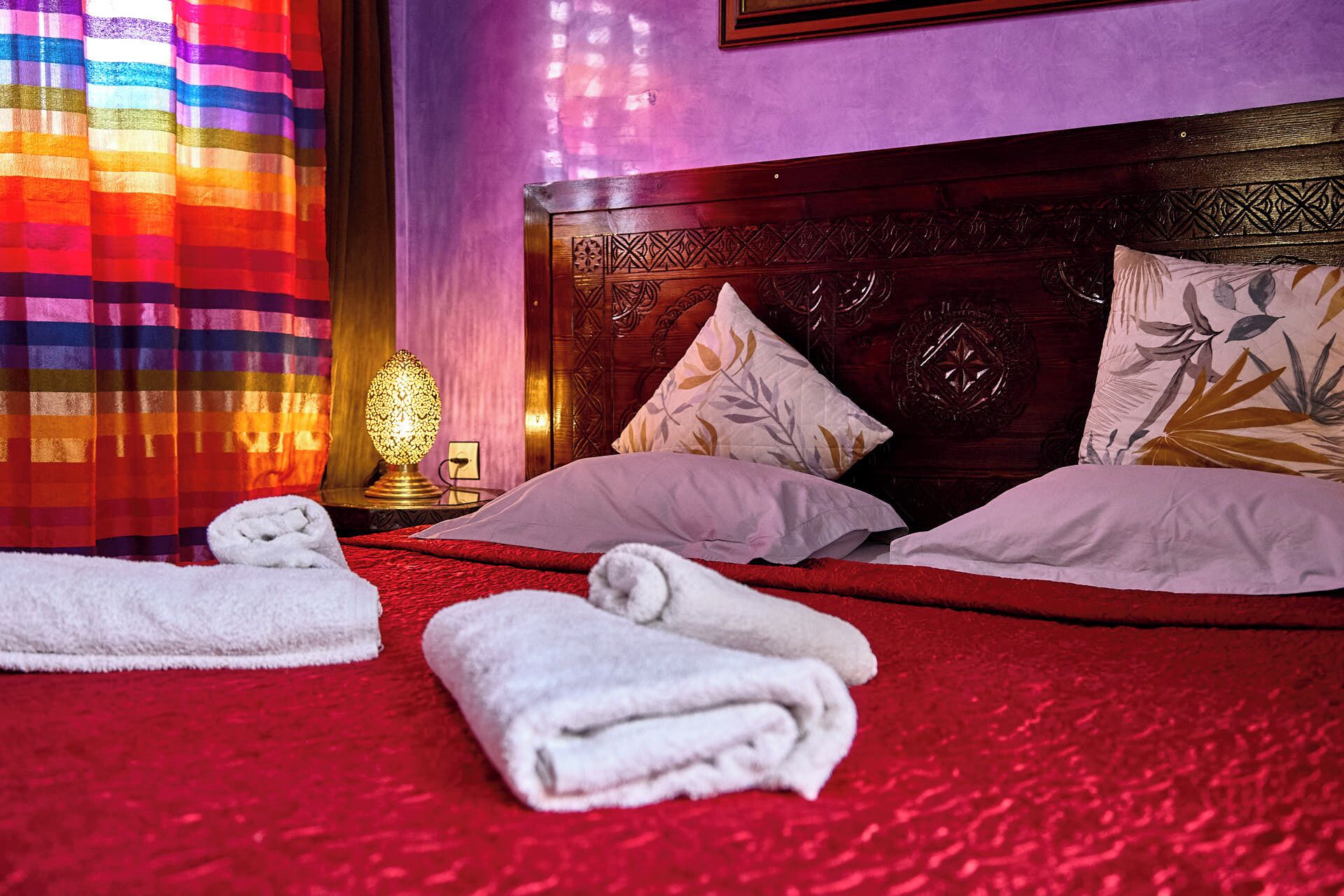 Une chambre d’hôtel avec une moquette rouge, une tête de lit en bois et deux oreillers ornés de motifs de feuilles.