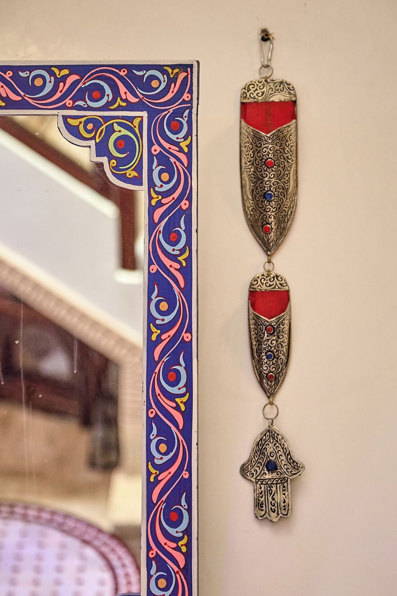 Un miroir décoratif doté d’un cadre coloré et d’un ornement suspendu aux motifs complexes.