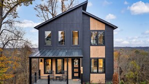 Een modern huis met twee verdiepingen, een donkere gevel, grote ramen en een houten veranda.