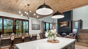 Een moderne keuken met een groot eiland, houten plafond en grote ramen met uitzicht op een bebost gebied.