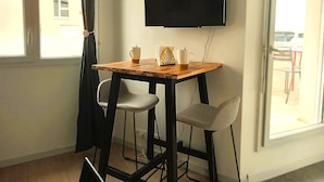 Ein Zimmer mit Holztisch, zwei Stühlen, einem flachbildfernseher an der Wand und einem Fenster mit Vorhängen.