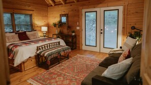 A cozy log cabin bedroom with a bed, bench, and a couch. - Scenic View Timber Lodge Hottub by Casa Oso (Mariposa)