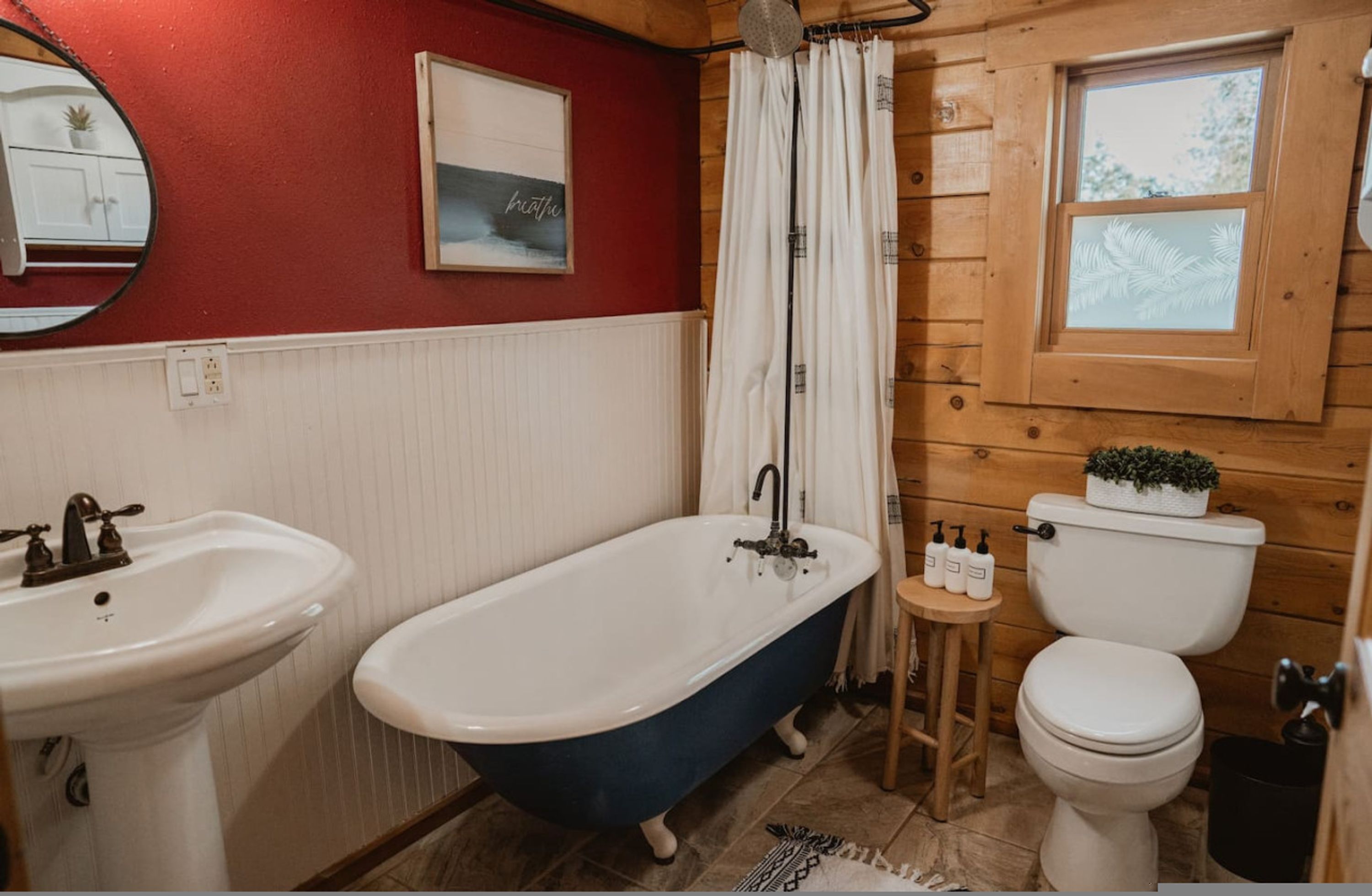 A bathroom with a clawfoot bathtub, a white sink, a toilet, and a small wooden stool with toiletries.