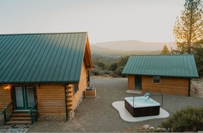 A log cabin with a hot tub and a smaller cabin, surrounded by a gravel driveway and a mountainous landscape. - Scenic View Timber Lodge Hottub by Casa Oso (Mariposa)