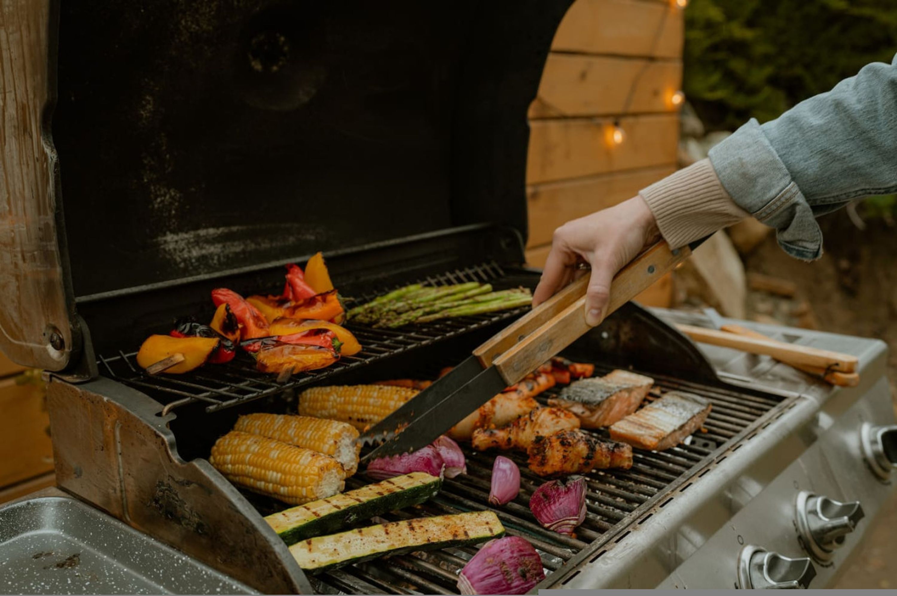 A person grilling a variety of vegetables and meats on an outdoor grill.