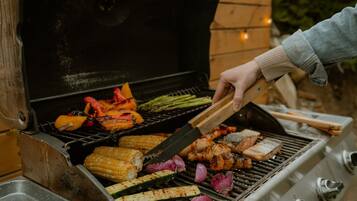 A person grilling a variety of vegetables and meats on an outdoor grill.