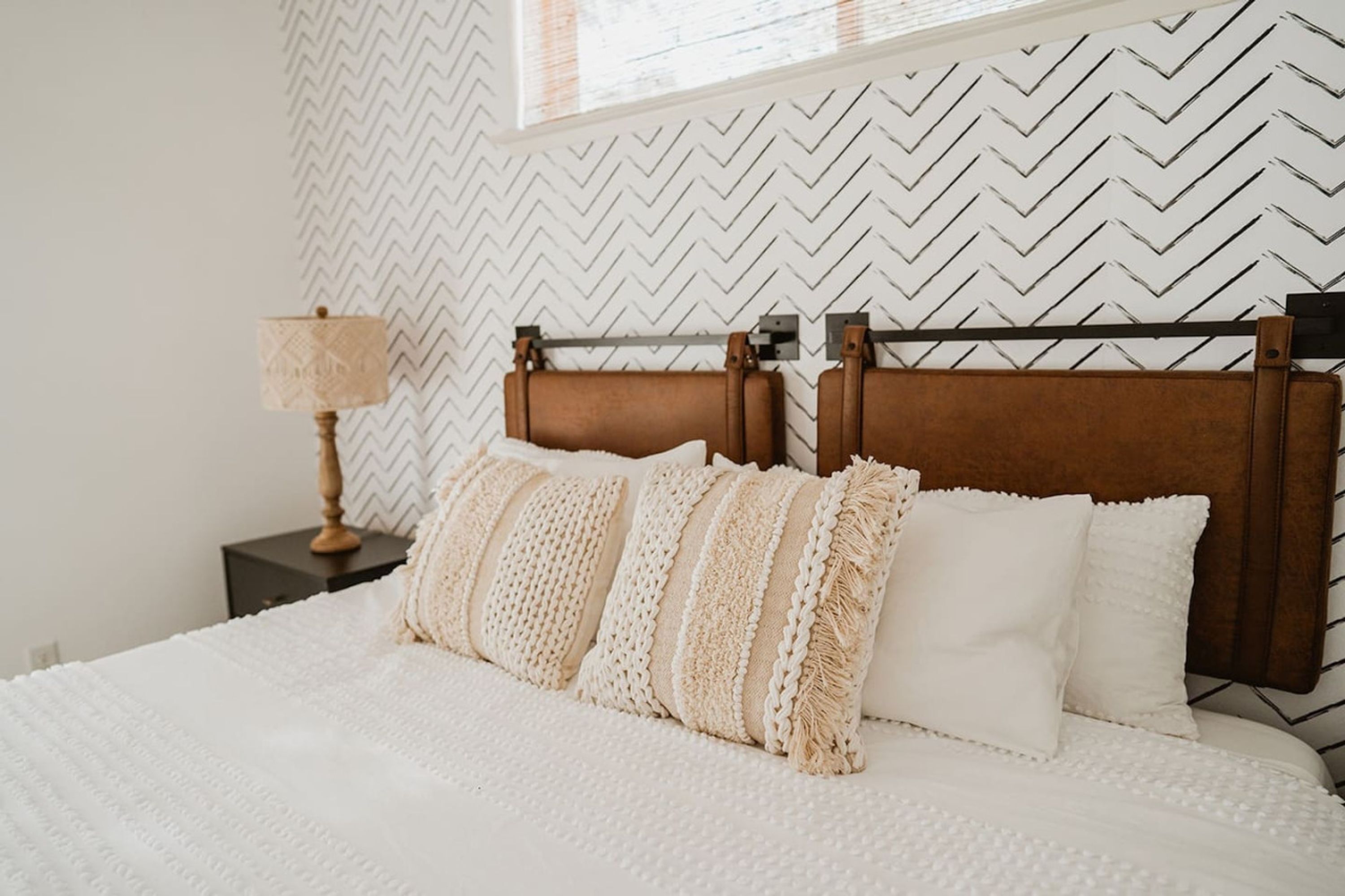 Un lit bien fait, avec une tête de lit en bois, une lampe de chevet et un mur décoré d’un motif.