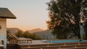 Uma área de piscina com degraus, espreguiçadeiras e vista para colinas.
