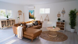 Uma sala de estar moderna com um sofá de couro marrom, uma mesa de centro redonda de madeira e um aparelho de ar condicionado branco na parede.