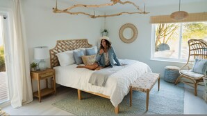 Quarto com cama, mesas de cabeceira, luminária pendente, janela com vista e uma cadeira.