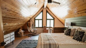 Ein gemütliches Schlafzimmer im Dachgeschoss mit einem großen Bett, einem Hängesessel und Blick durch ein hohes Fenster.
