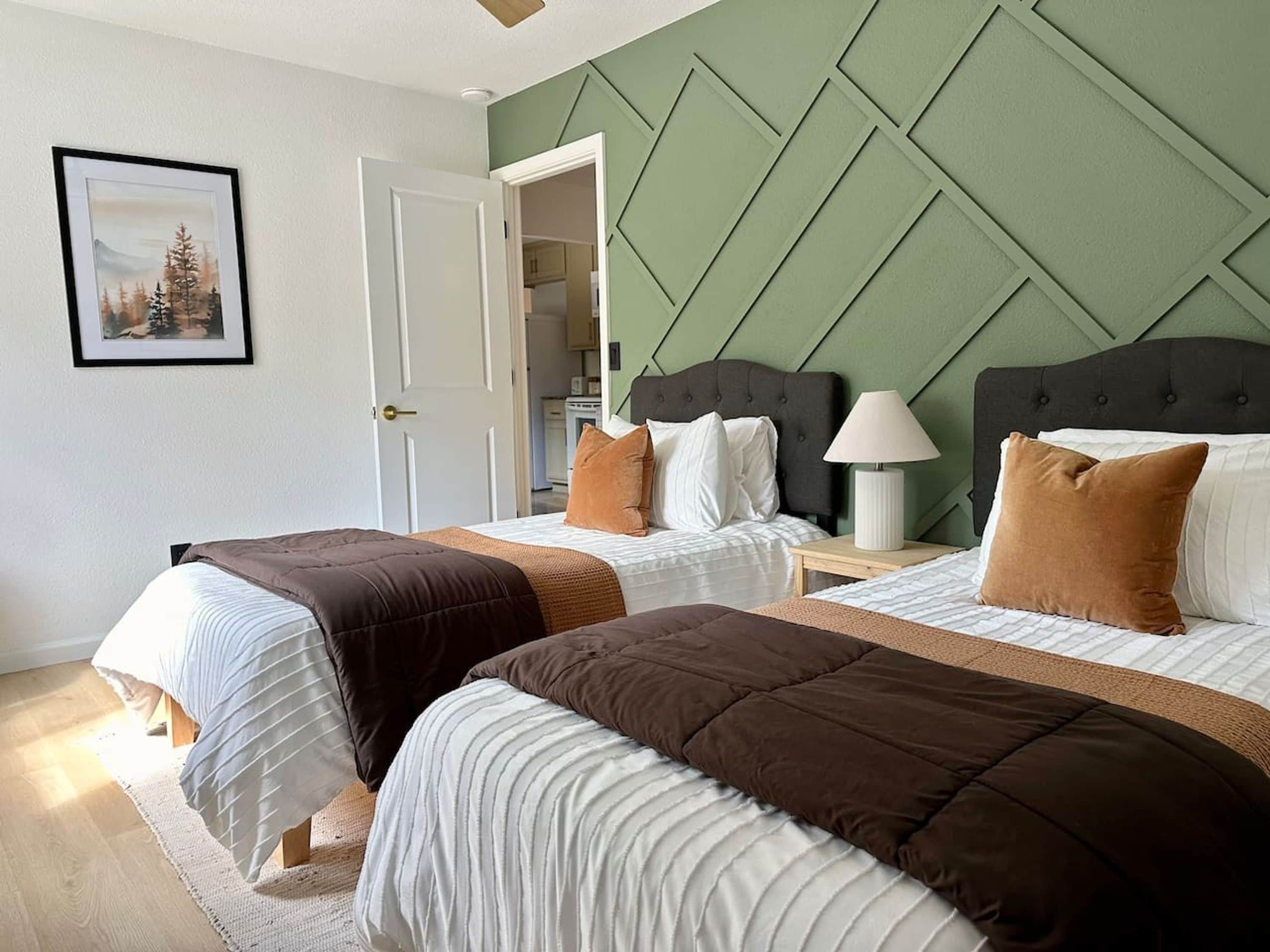 Quarto de hotel com duas camas, uma parede de destaque verde e um quadro na parede.
