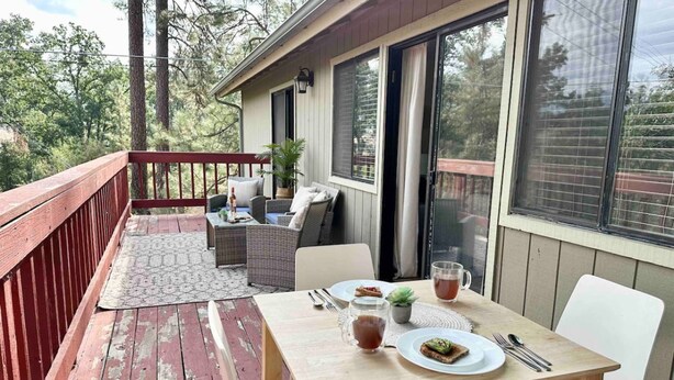 A wooden deck with a dining table and chairs, a small potted plant, and a window with a view of trees. - Prime Location Yosemite Adventure by Casa Oso (Oakhurst)