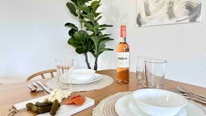 A dining table set with white plates, bowls, cutlery, and glasses, with a bottle of wine and a plant in the background. - Prime Location Yosemite Adventure by Casa Oso (Oakhurst)