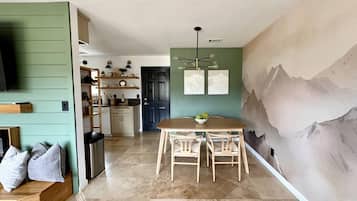 Una cocina moderna con comedor, televisor montado en la pared y un mural de montañas.