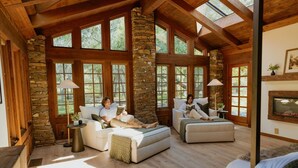 A spacious living room with stone walls, large windows, and wooden beams. There are two sofas and a fireplace. - Stone House I Thoughtful Nature Stay Near Yosemite (Mariposa)