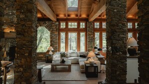 A spacious living room with stone pillars, a fireplace, and large windows offering a view of the outdoors. - Stone House I Thoughtful Nature Stay Near Yosemite (Mariposa)
