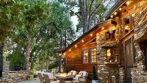 A log cabin with a stone exterior, outdoor seating area with chairs and a fire pit, surrounded by trees. - Stone House I Thoughtful Nature Stay Near Yosemite (Mariposa)