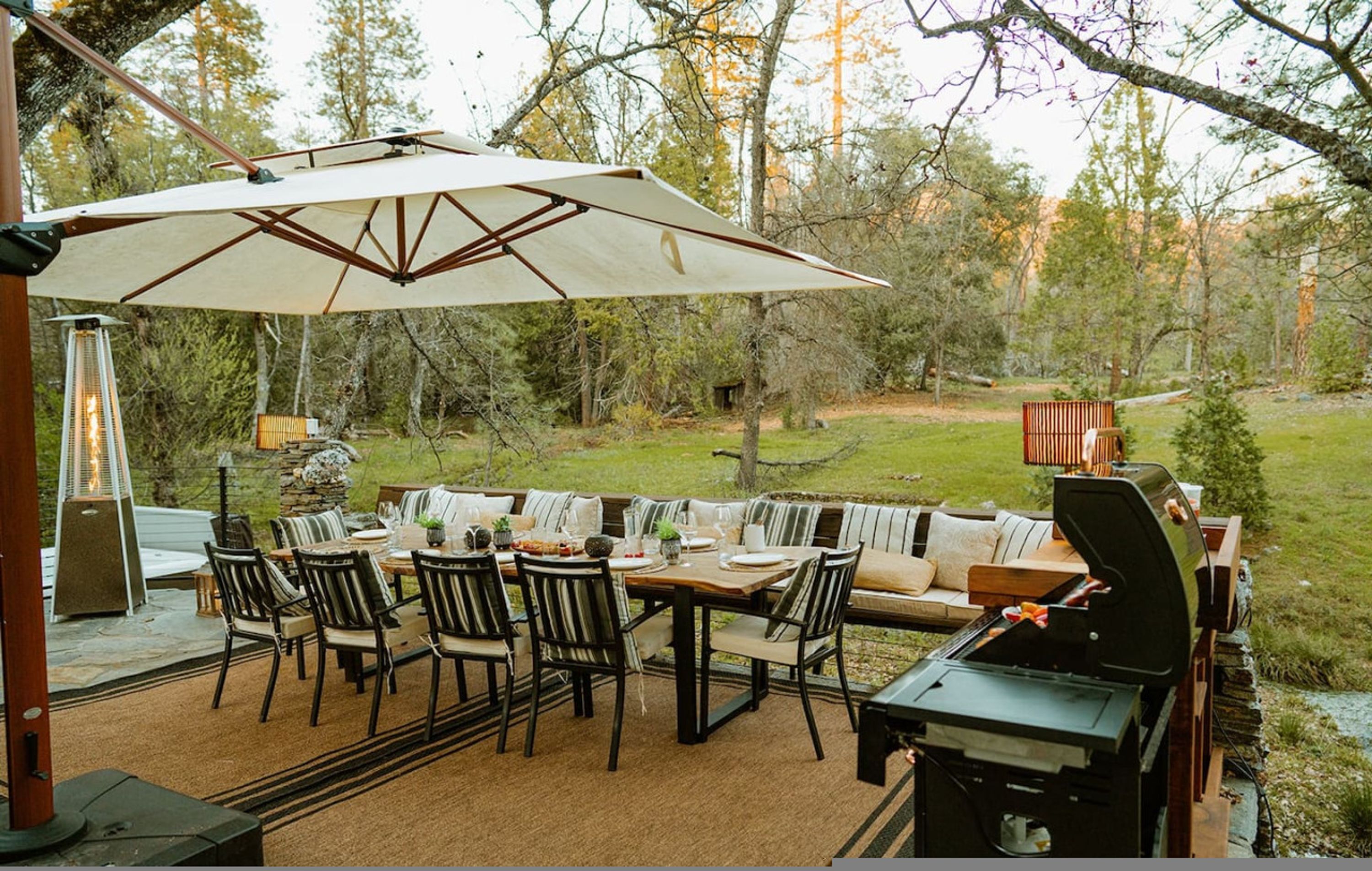 An outdoor patio with a dining table, chairs, a large umbrella, a grill, and a cozy seating area.