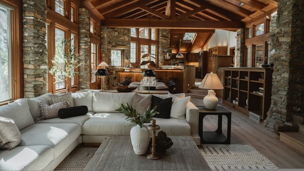 A spacious living room with a large sectional sofa, a coffee table, and a fireplace. The room features exposed wooden beams, stone walls, and large windows. - Stone House I Thoughtful Nature Stay Near Yosemite (Mariposa)