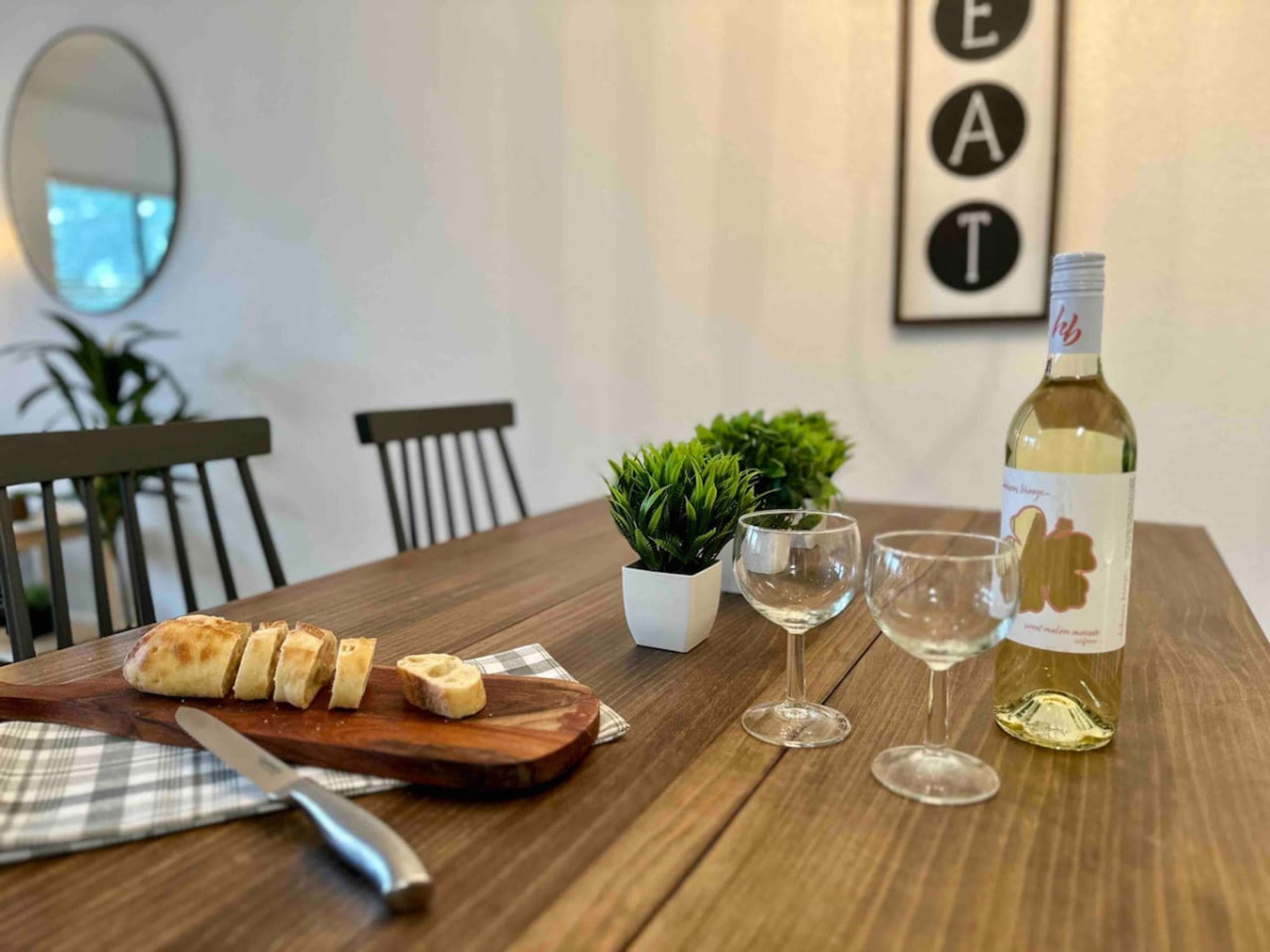 A wooden dining table with a loaf of bread, two wine glasses, and a bottle of wine.