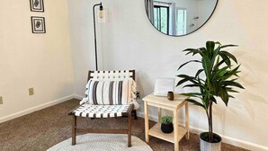 A room with a round mirror, a chair with striped cushions, a small table with a vase, and a potted plant. - Prime Location Yosemite Expedition by Casa Oso (Oakhurst)