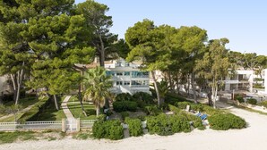 A coastal hotel with multiple floors, surrounded by lush greenery and a sandy beach. - Casa Ketilla, front line apartment (Alcúdia)