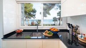 A kitchen with a view of the sea, a sink, and various kitchen items on the counter. - Casa Ketilla, front line apartment (Alcúdia)