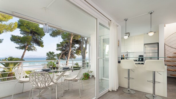 A modern kitchen with a view of the sea, a balcony with white chairs, and a dining table. - Casa Ketilla, front line apartment (Alcúdia)