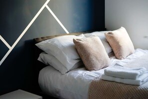 A neatly made bed with white linens and two textured pillows, set against a wall with a geometric pattern. - Spacious House for 12 Near Madejski Stadium & M4 (Berkshire)