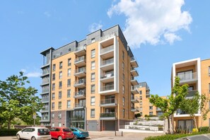 A multi-story residential building with balconies, a parking area, and a clear sky.