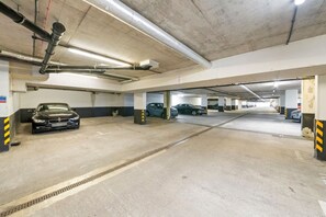 A multi-level underground parking garage with concrete floors and walls, featuring several parked cars and visible structural elements like columns and overhead pipes.