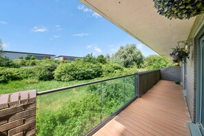 A balcony with a wooden floor, glass railing, and a view of greenery and buildings. - Spacious Retreat for 7 with 2 Bathrooms (Berkshire)