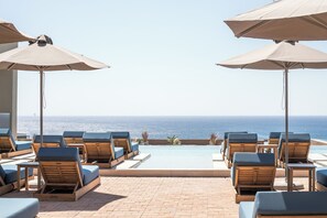Un espace aménagé au bord de la piscine, avec des chaises longues et des parasols, offrant une vue sur l’océan.