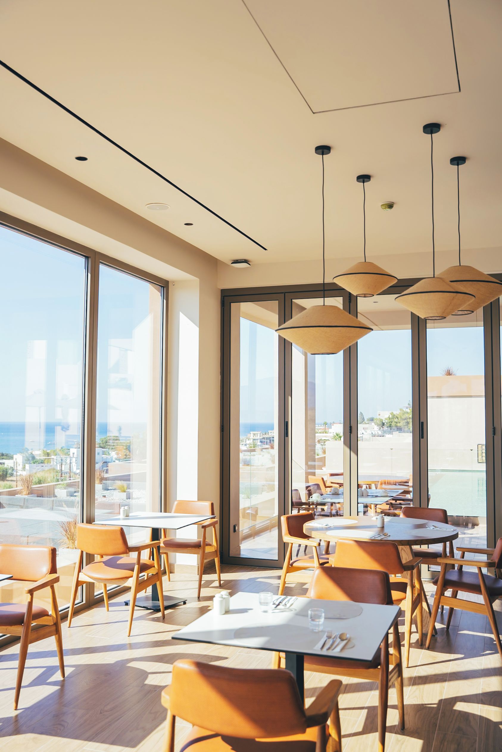 Un comedor moderno con ventanas amplias, varias mesas y lámparas colgantes.
