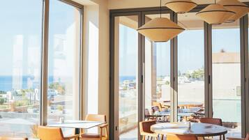 Un comedor moderno con ventanas amplias, varias mesas y lámparas colgantes.