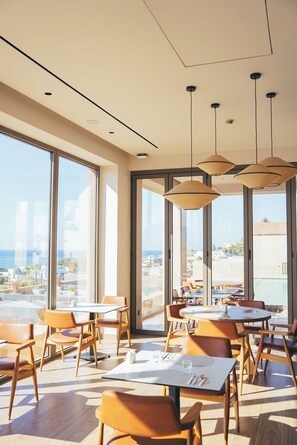 Un espace de restauration moderne doté de grandes fenêtres, de nombreuses tables et de luminaires suspendus.