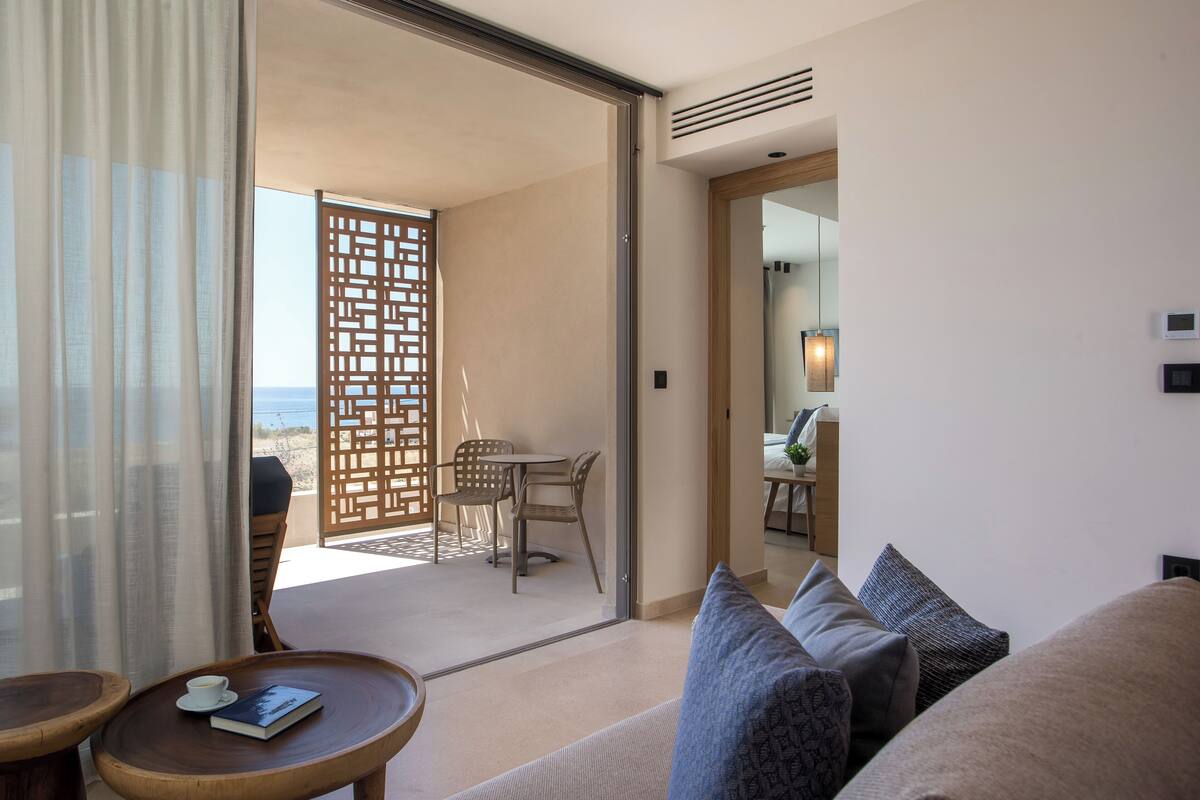 Une chambre d’hôtel avec un balcon, un canapé, une petite table avec un livre et une tasse, et une vue sur la plage.