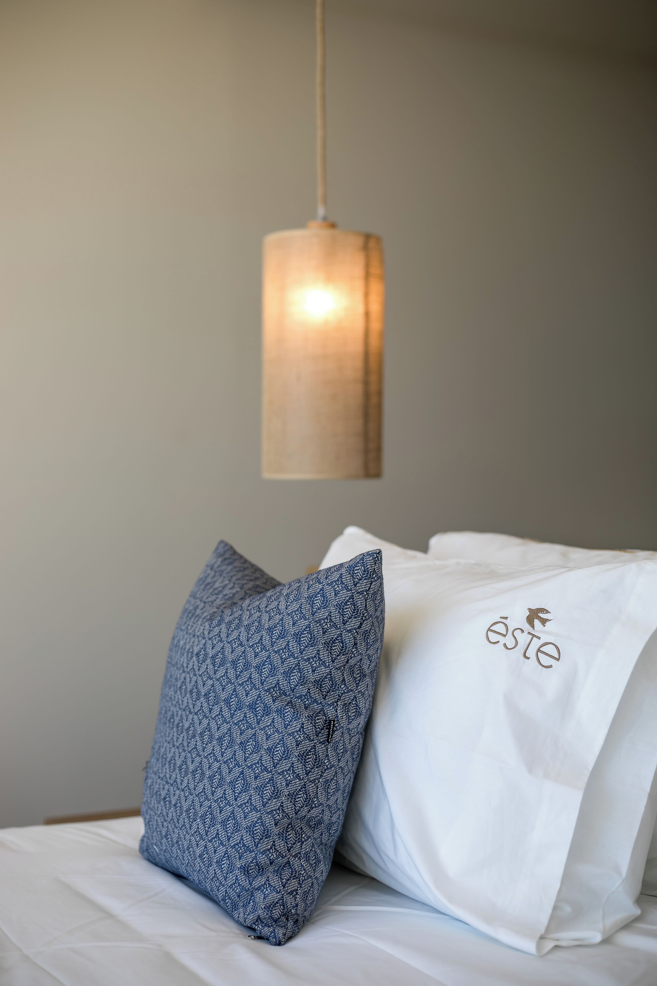 A bed with a blue patterned pillow and a white pillow with a logo.
