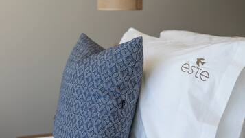 A bed with a blue patterned pillow and a white pillow with a logo.