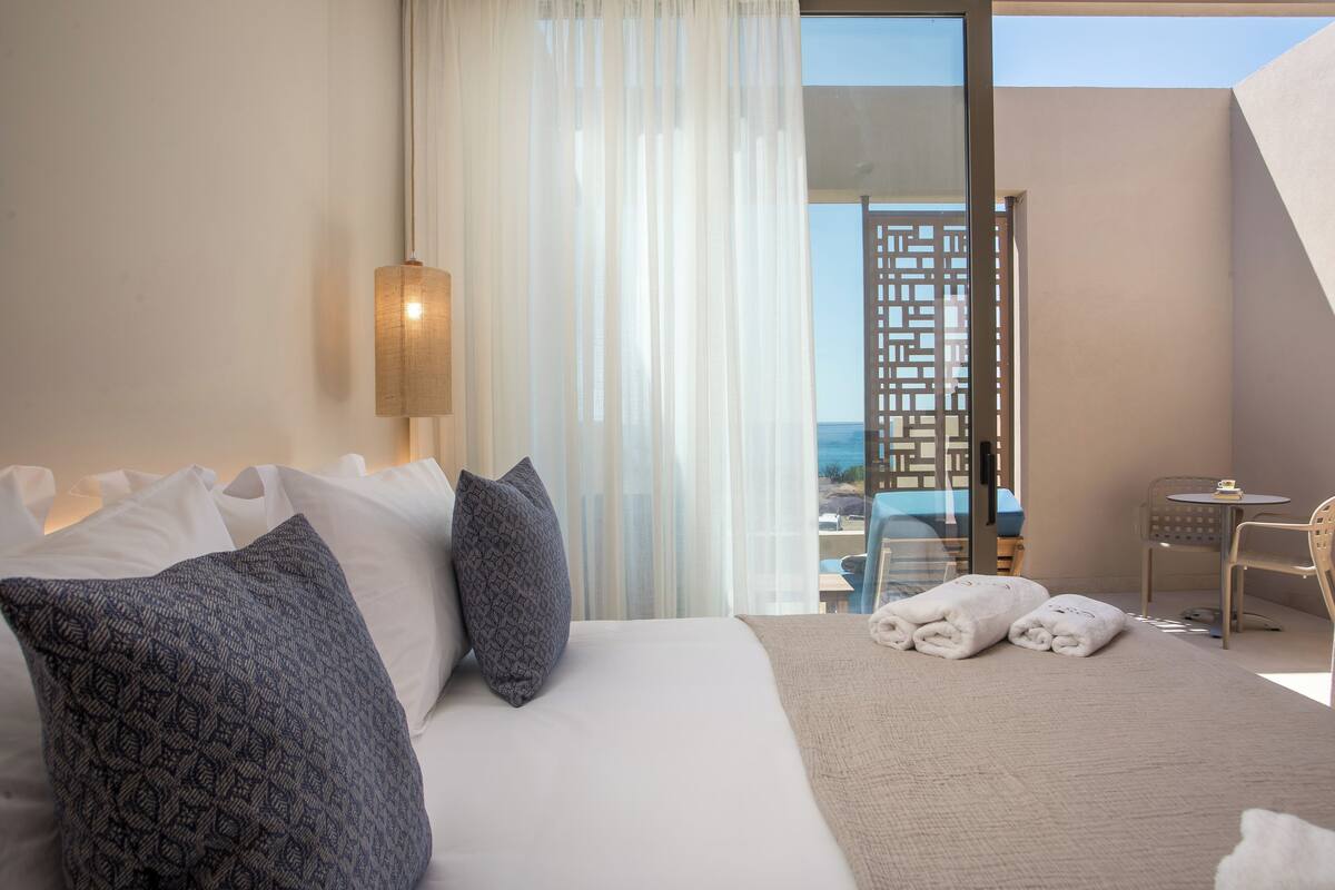 Une chambre d’hôtel avec un grand lit, une petite table et une vue sur la ville, visible à travers une porte vitrée.