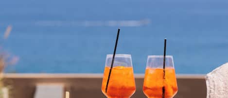 A table with a burger, fries, and a salad, and two glasses of orange drink, overlooking the ocean.