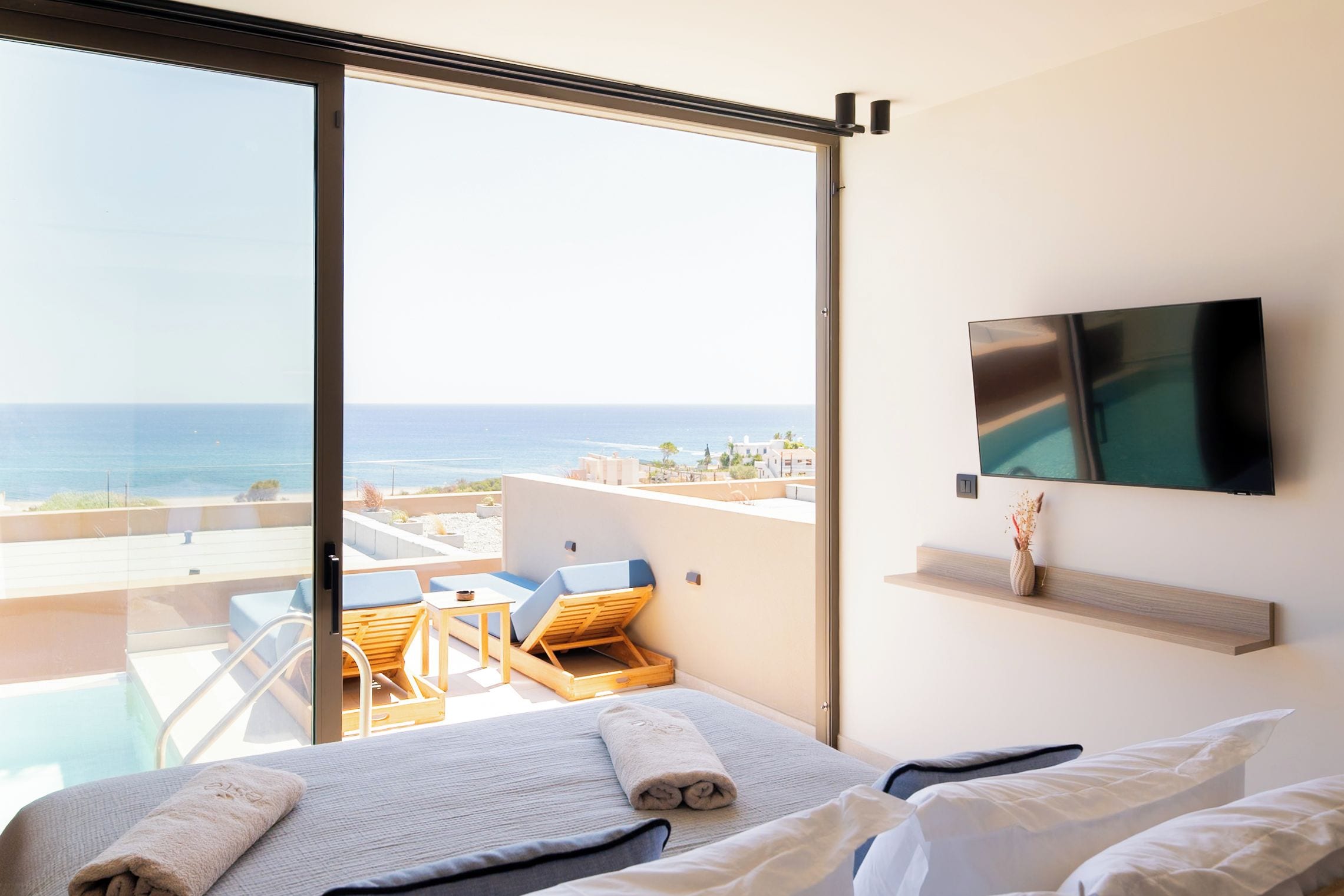 Habitación de hotel con cama, televisión, balcón con vista al mar y mesa con sillas.