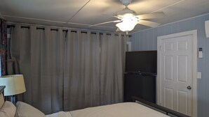 A bedroom with a bed, a ceiling fan, a television on a stand, and a door. - Charming, treetop Indian River Hideaway (Cocoa)
