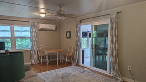 A cozy living room with a ceiling fan, a round table with chairs, a sofa, and a large window with curtains. - Charming, treetop Indian River Hideaway (Cocoa)